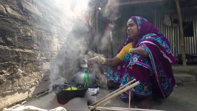 女人在传统的粘土炉上做饭，跟踪从火和炒锅中射出的东西。