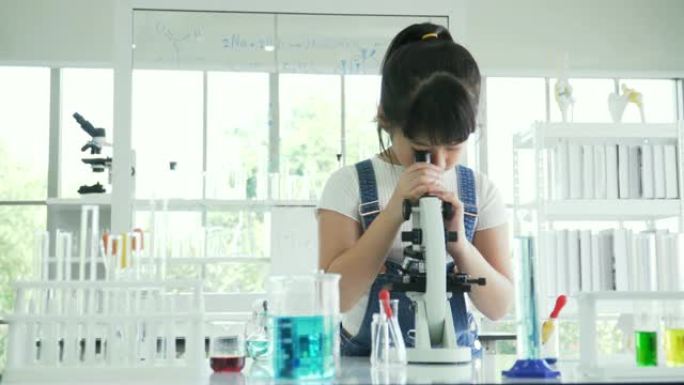 dolly拍摄的前视图: 好奇的亚洲女孩根据自己的意愿调整光学显微镜