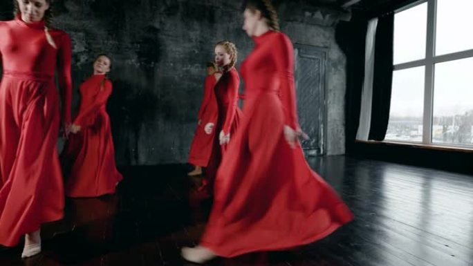 一群年轻的舞者女孩穿着红色长裙在黑暗的大厅里排练，表演