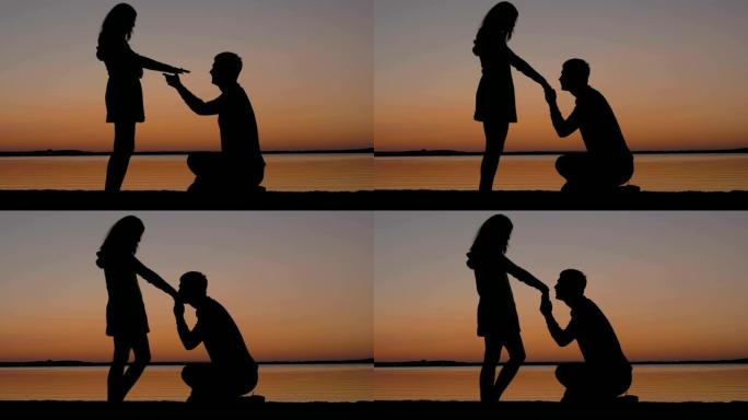 男人坐在膝盖上，然后拉着女人的手，在日落时亲吻她