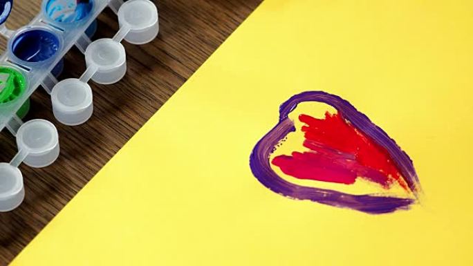 孩子画画。一个小女孩的手在黄纸上画了一颗五颜六色的心。