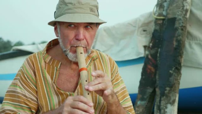 渔船旁的沙滩上玩竹笛的老人肖像