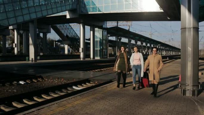 三个带着行李箱的女人走上火车站的平台聊天。