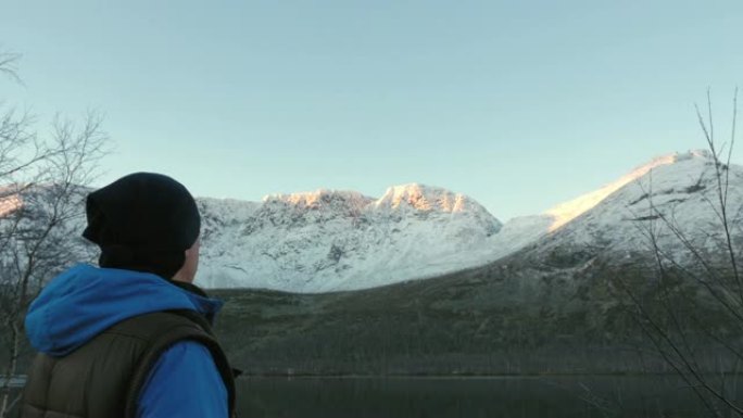 一个男人，一个中年运动员，在山里遇见黎明。他非常欣赏太阳和湖中山脉的反射。