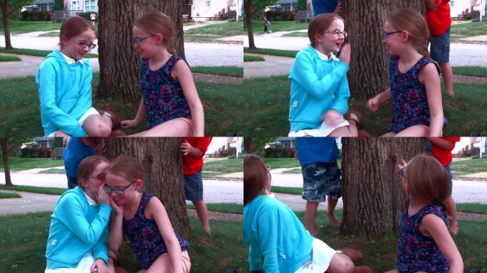 两个女孩在前院的一棵树旁互相告诉秘密，两个小男孩偷偷溜到后面，给他们一个惊喜