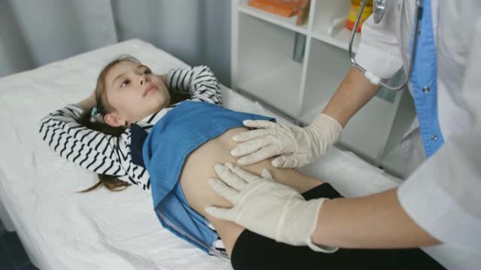 女医生在医疗办公室近距离触诊了一个小女孩病人的腹部。