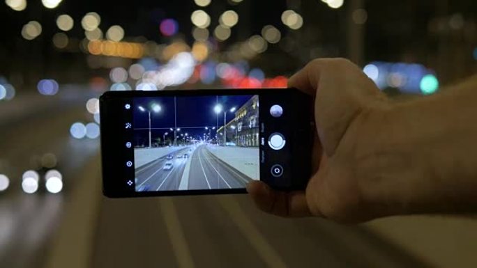 一个人的手握着智能手机，可以消除汽车的运动。在城市街道模糊灯光的背景下。