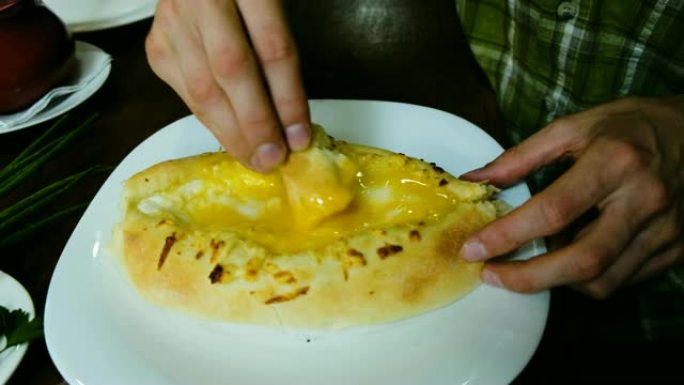 男人正在吃格鲁吉亚国家菜-khachapuri。这家伙把一块面包打碎，蘸上奶酪和黄油的特写。