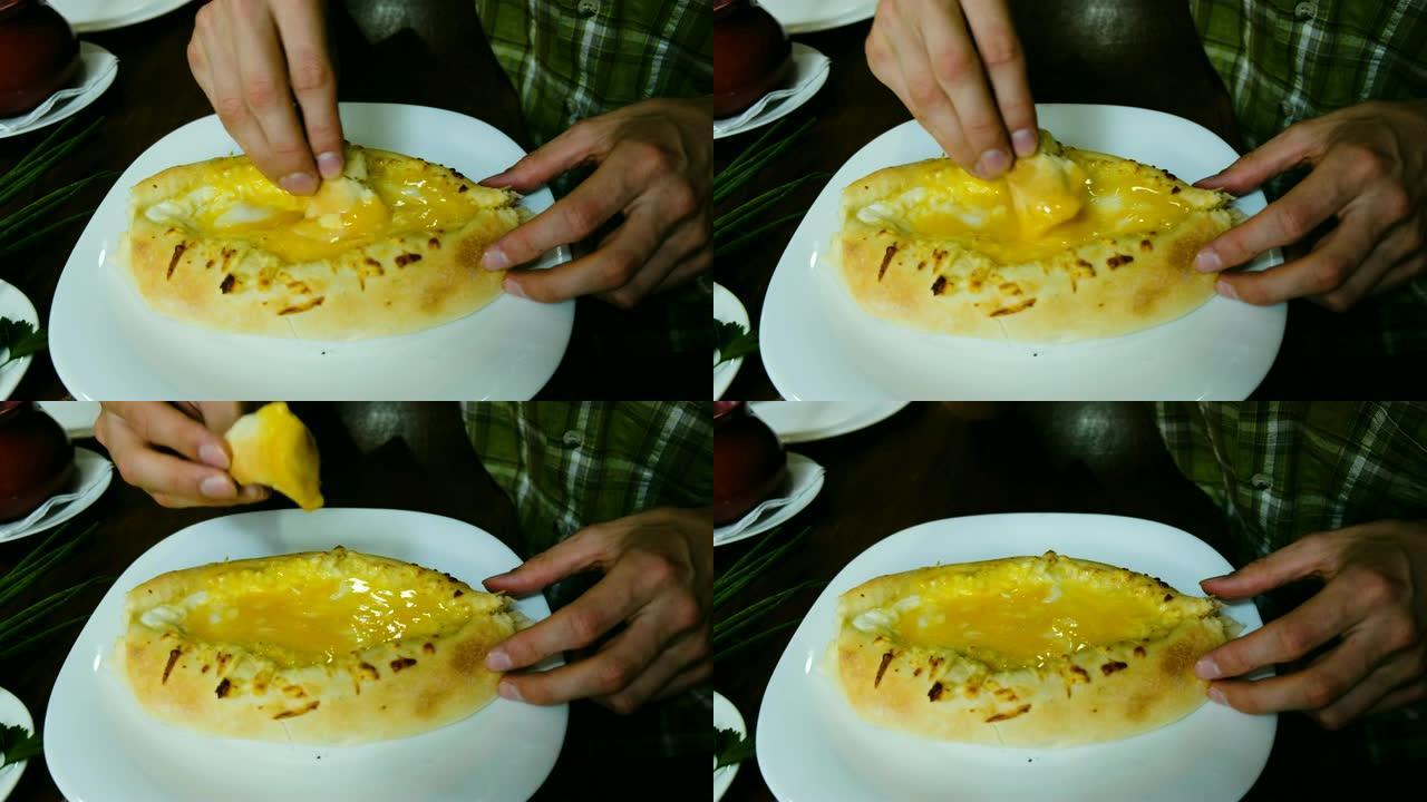 男人正在吃格鲁吉亚国家菜-khachapuri。这家伙把一块面包打碎，蘸上奶酪和黄油的特写。