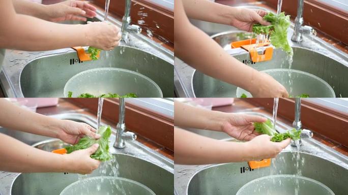 4k镜头。女人从新鲜的生菜中取出并沥干水，从柜台厨房的水槽中清洗蔬菜，准备烹饪原料