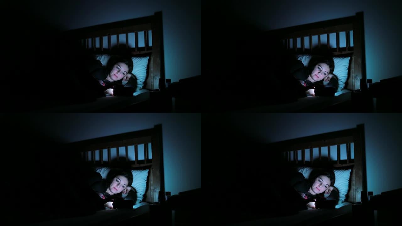 躺在床上的年轻女子带着智能手机。女人在4k睡觉前在手机设备上主演