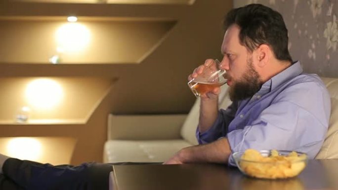 男人看足球比赛，自己倒啤酒，吃薯片