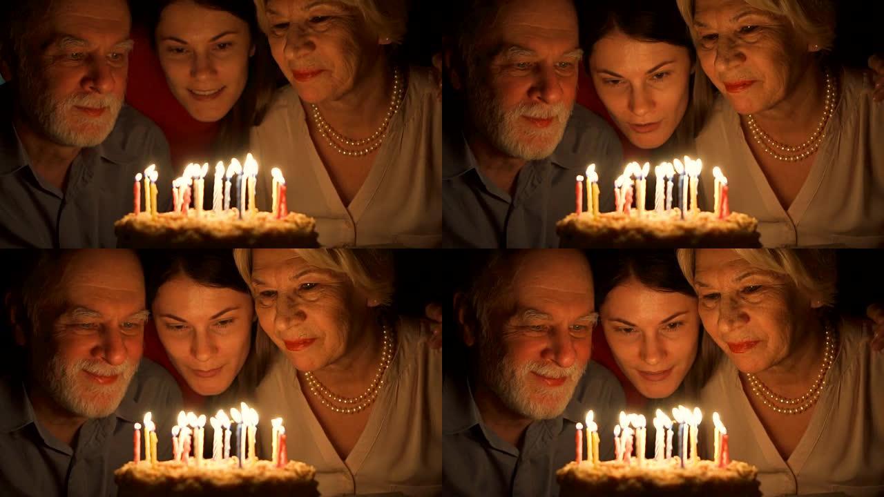 充满爱心的高级夫妇和他们的女儿在家用蛋糕庆祝。拥抱和吹灭蜡烛