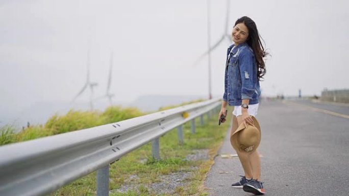 慢动作，亚洲女性游客快乐地行走。背景是旋转风力涡轮机。