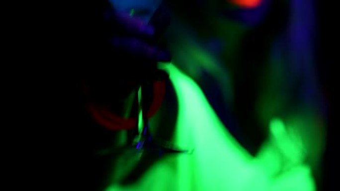 蓝色发光饮料与跳舞的女人在紫外线发光派对背景和女人来拿饮料。。
