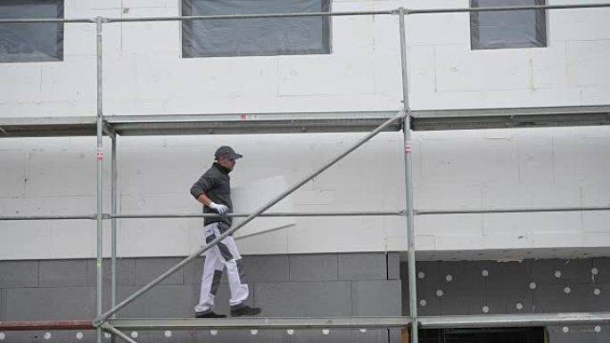 在脚手架上使用外部建筑隔热材料的高加索工人。