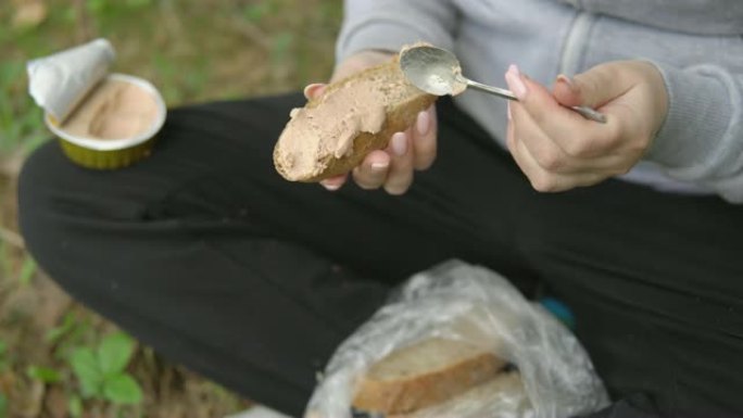 年轻女子在一块面包上撒上酱。徒步旅行中的小吃