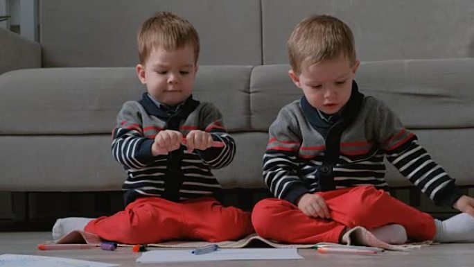 两个双胞胎兄弟蹒跚学步的孩子坐在地板上画标记。