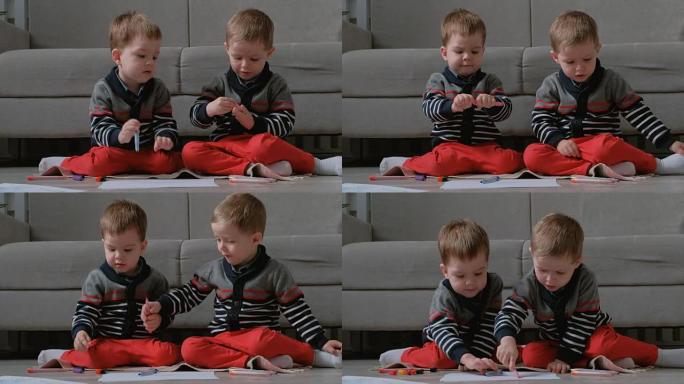 两个双胞胎兄弟蹒跚学步的孩子坐在地板上画标记。