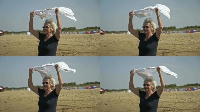 在多风的海滩上，头顶白衬衫的高级妇女
