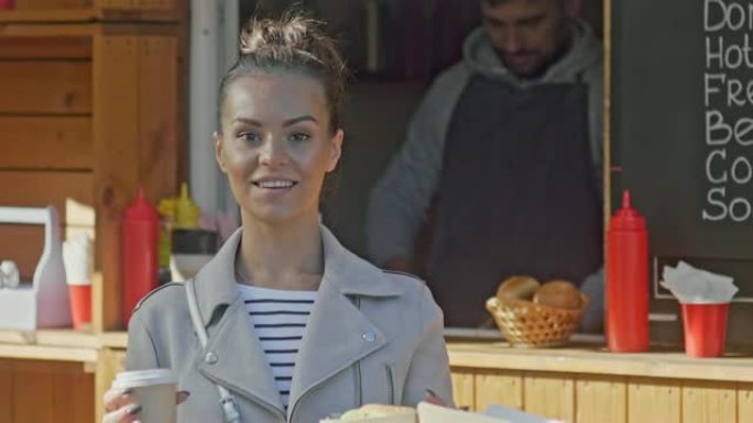 微笑的女人站在食品亭附近喝咖啡