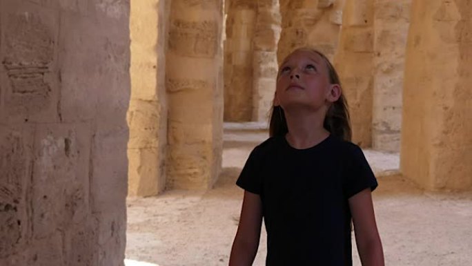 步行女孩在走廊上抬头和四处张望，拱门和柱子是米色的
