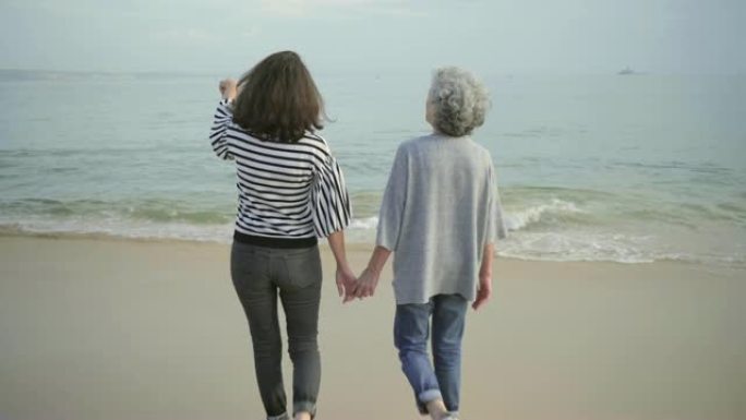 两个快乐成熟的女士在沙滩上散步时手牵在一起的背景图。