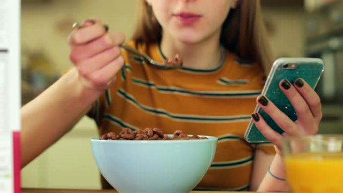 十几岁的女孩在手机上吃不健康的一碗含糖早餐麦片发短信