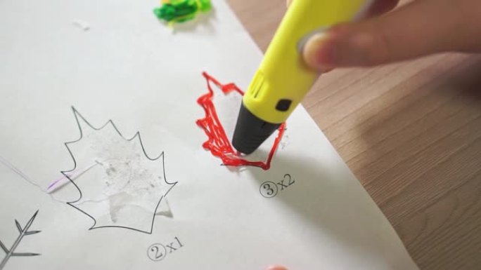 特写男孩的手使用3D笔。他用红色ABS塑料创造了一片植物叶子。