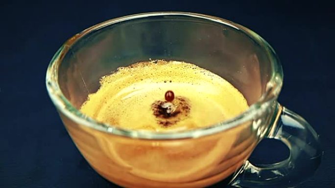 咖啡滴以慢动作掉落在trasparent杯意式浓缩咖啡中，黑光背景上有泡沫，食物和饮料并放松