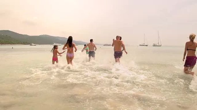 一群家人朋友疯狂地跑进海里的慢动作视图，后视图。