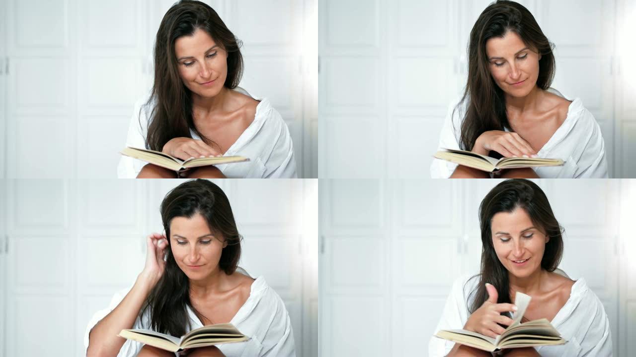 肖像的微笑漂亮的女人看书和翻页坐在床上的卧室