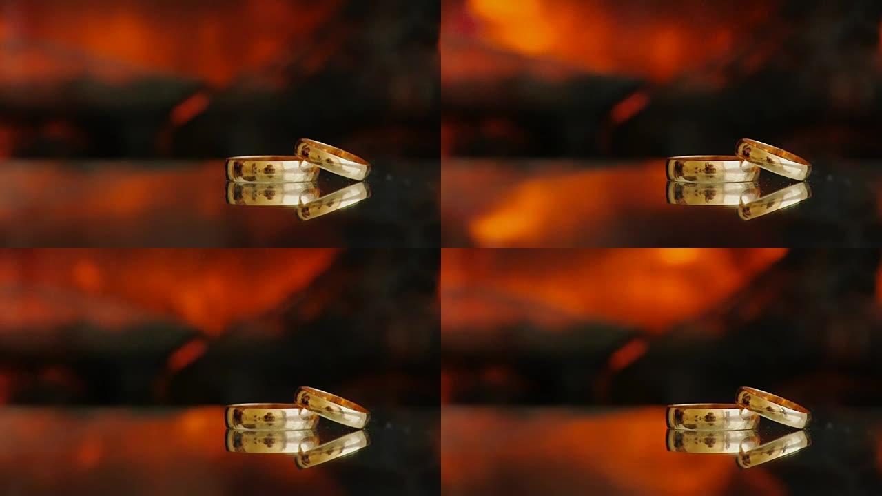 静态框架两个金戒指对着壁炉玻璃桌子上的火黑色深色背景