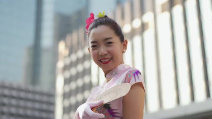 穿着粉色chipao的中国女人微笑着拿着风扇。