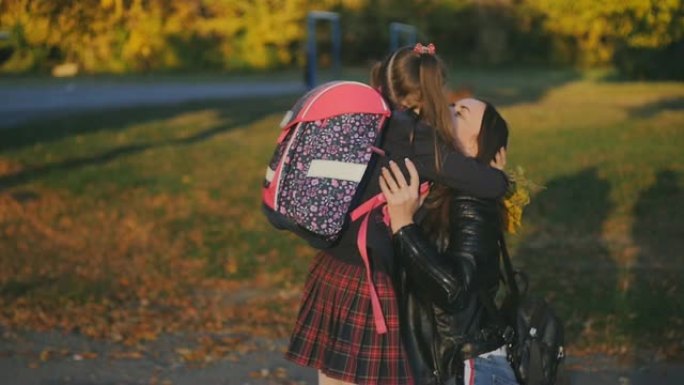 妈妈在学校遇见了她的小女儿。穿着校服的女孩背着背包跑向母亲。慢速射击