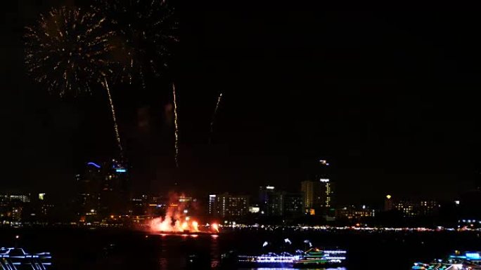 天空中真正的烟花节的4k镜头，用于夜间庆祝，背景为城市景观，海岸一侧前景为海上漂浮的船只