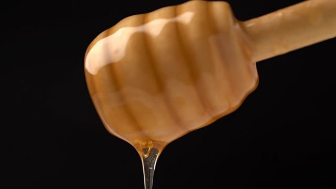黑色背景上的有机蜂蜜从木制蜜勺中滴下的镜头