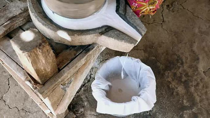 女人盘腿坐着，用手翻磨石磨湿米饭，制成浸泡的米粉