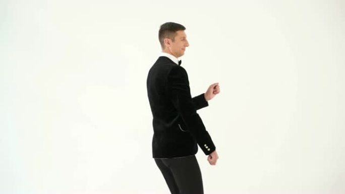 穿着黑色西装打着领结的有趣男人正在白色背景上展示舞者的舞蹈