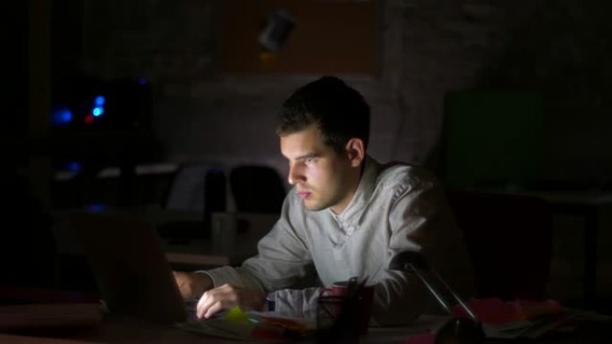 集中的高加索男性正在看电脑屏幕和键盘打字，在桌面工作，深夜，黑暗的背景