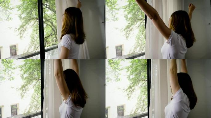 年轻美丽的亚洲女人早上醒来靠近窗户伸展