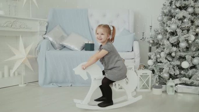 非常漂亮的小女孩在新年的房间里骑着一匹木马，微笑着