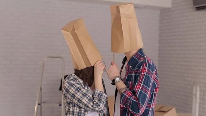 新婚夫妇在他们的新公寓里玩得开心，头上装着纸板袋。