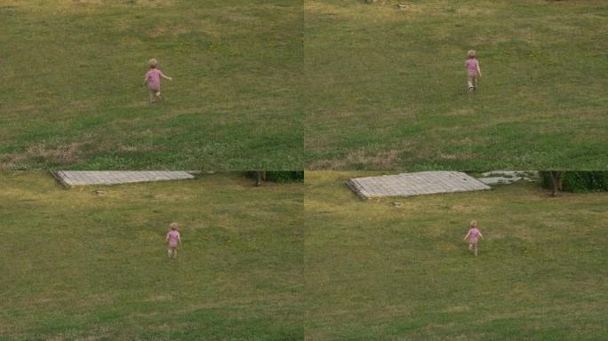一个小男孩在公园的绿草地上奔跑，他从山上跑下来。