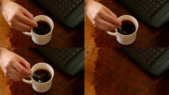 用手在白色杯子里搅拌黑咖啡，然后在木制办公桌上拿起