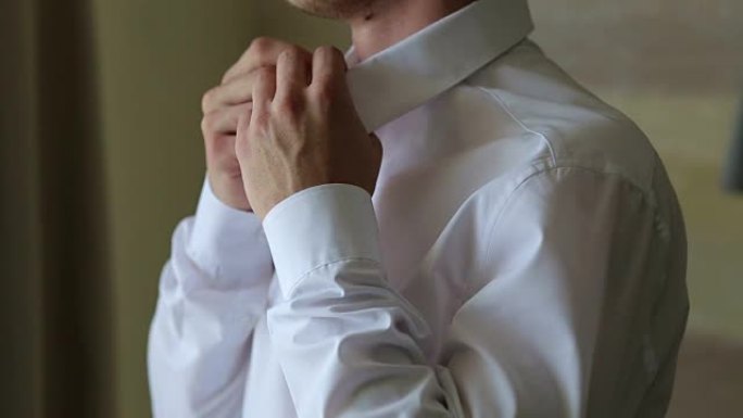 男人站在明亮的窗户前扣上他的白衬衫。特写