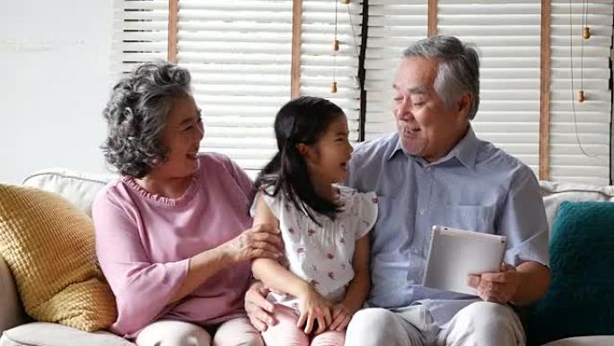 小女孩在玩平板电脑时与高级男人和女人拥抱。孩子带着快乐的情感和高级男女一起玩。有家庭、生活方式、科技