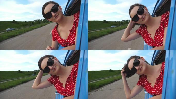 戴着墨镜的年轻女孩的肖像斜靠在老式车窗外，享受旅行。女人从移动复古汽车中望出去。旅游概念。穿着旧车的