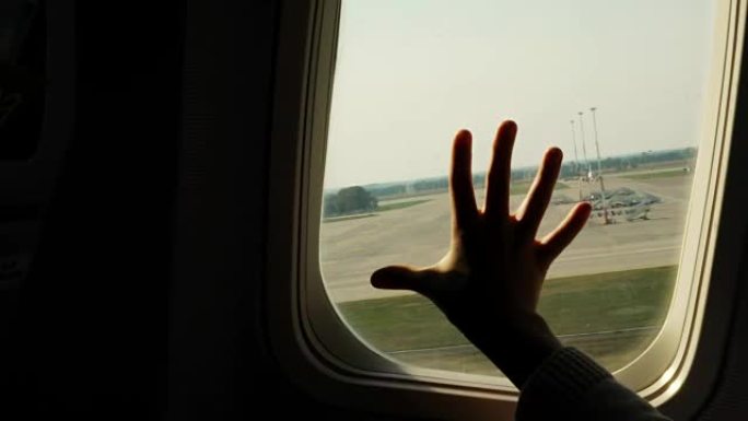 孩子的手触摸飞机窗户，特写。飞机窗户背景下儿童手掌的轮廓。飞行安全的概念
