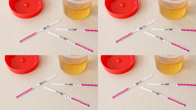 三个阳性妊娠试验结果，两张试纸放在桌子上。在尿罐旁边。
